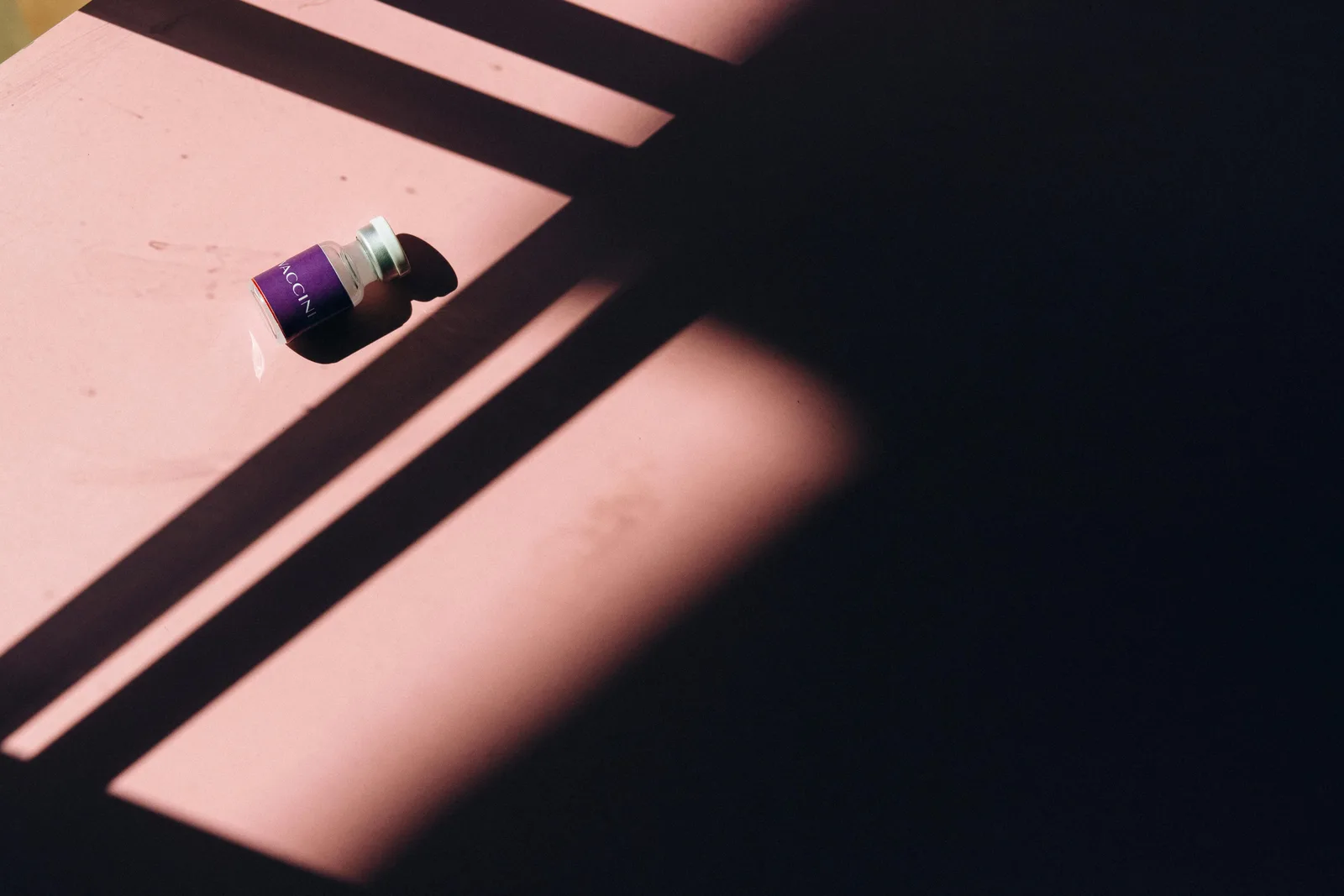 Cross-marker patterns: An artistic photograph of a vaccine vial amidst striking light and shadow patterns, emphasizing healthcare themes.