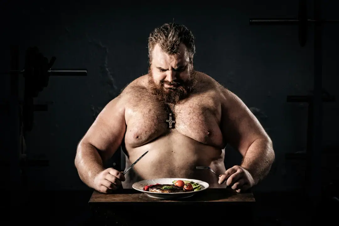 Anabolic resistance and per-meal leucine: Shirtless muscular man eating a nutritious meal, symbolizing strength and health.