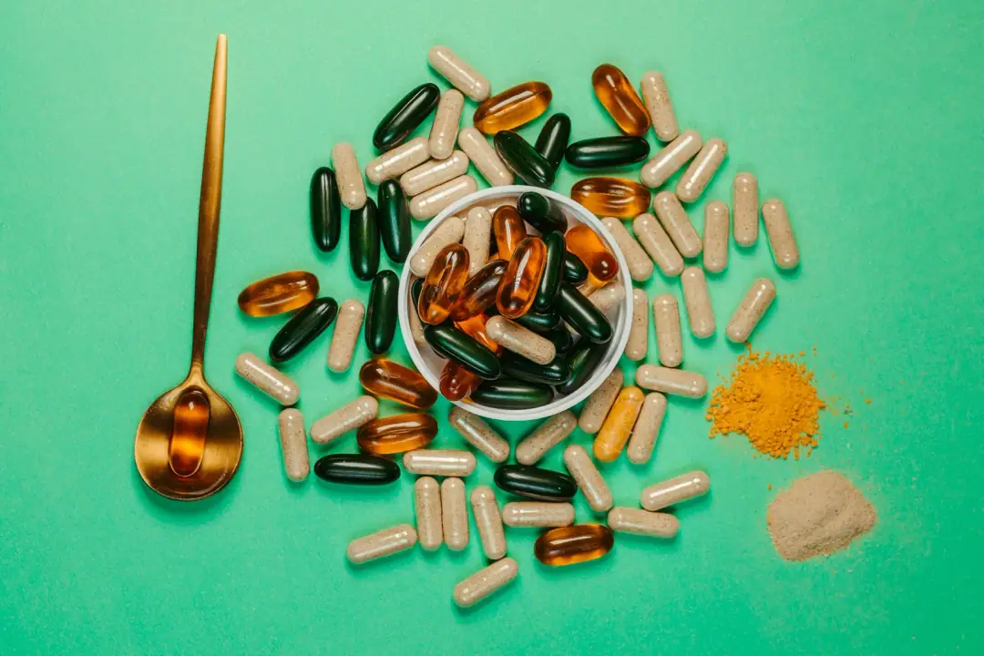 Tier-A foundation: the boring four: A vibrant assortment of capsules and powders on a green background with a golden spoon.