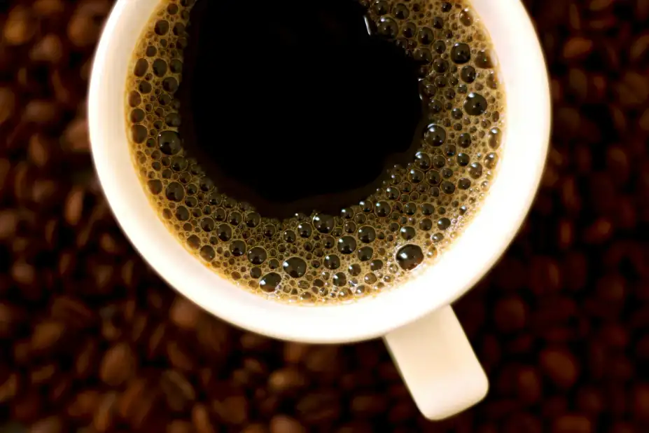 Counter-view: High-angle view of hot black coffee with bubbles in a white porcelain cup over coffee beans.