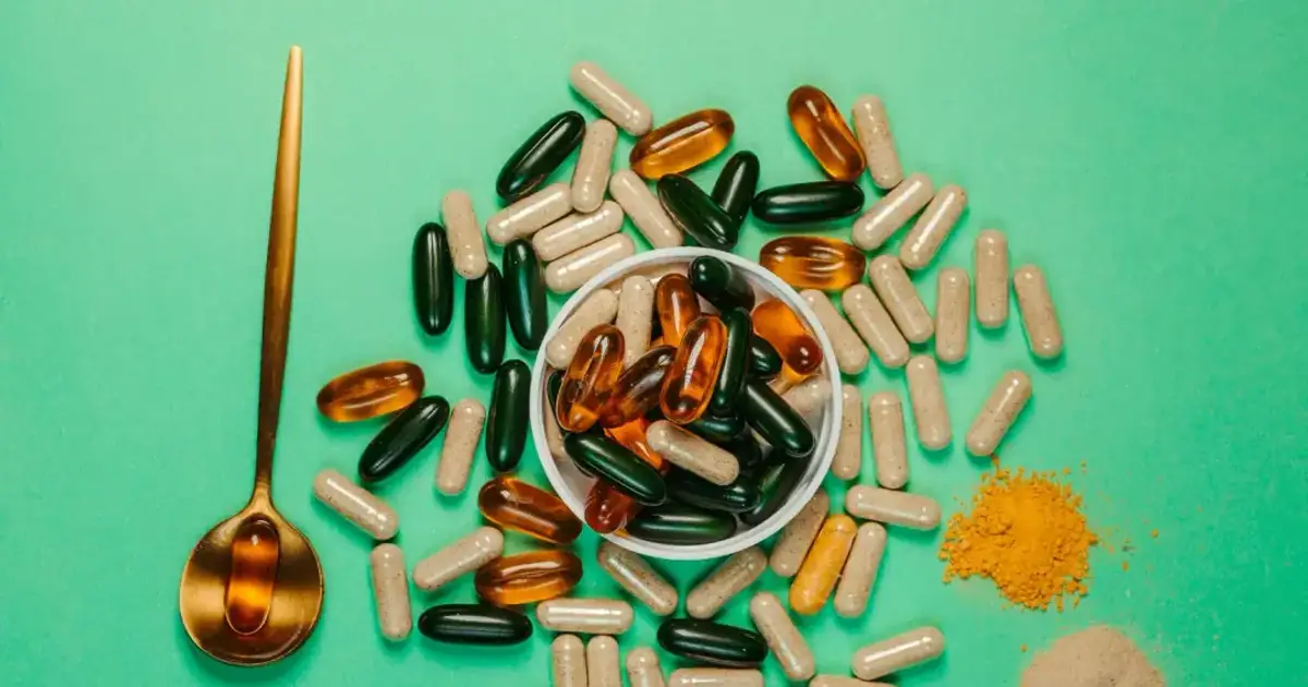 A vibrant assortment of capsules and powders on a green background with a golden spoon.