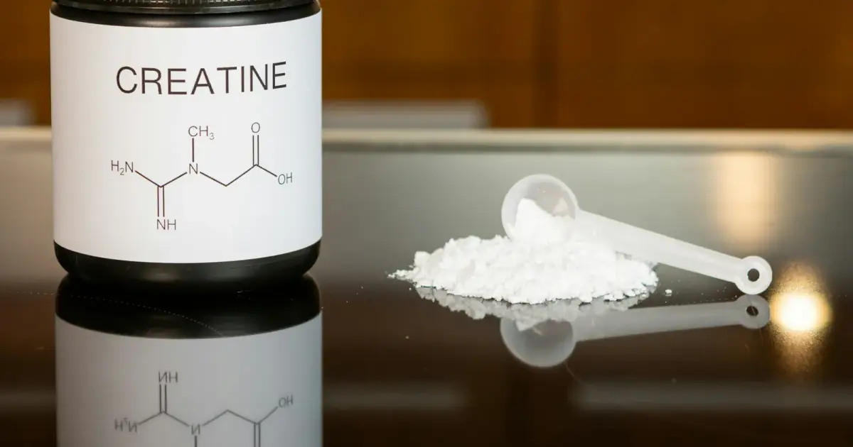 a bottle of creatine next to a spoon on a table