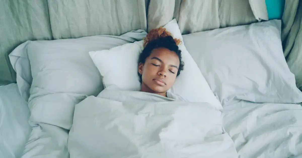 A young woman sleeping peacefully in a white bed.