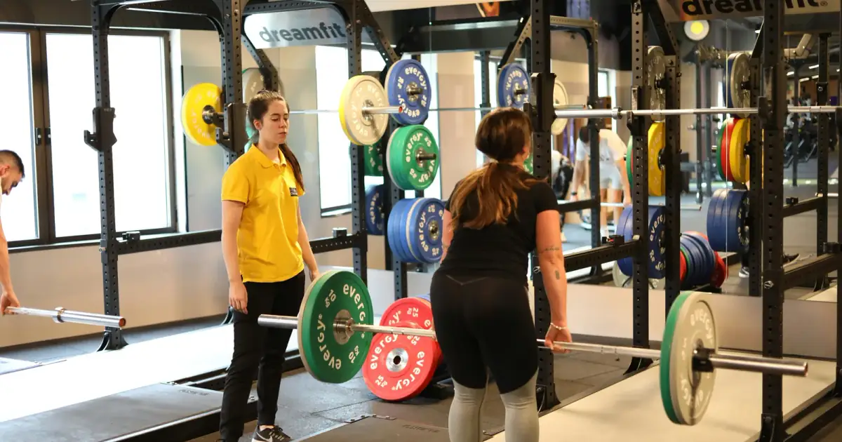 Two women weightlifting in a modern gym with colorful plates, showcasing fitness training.