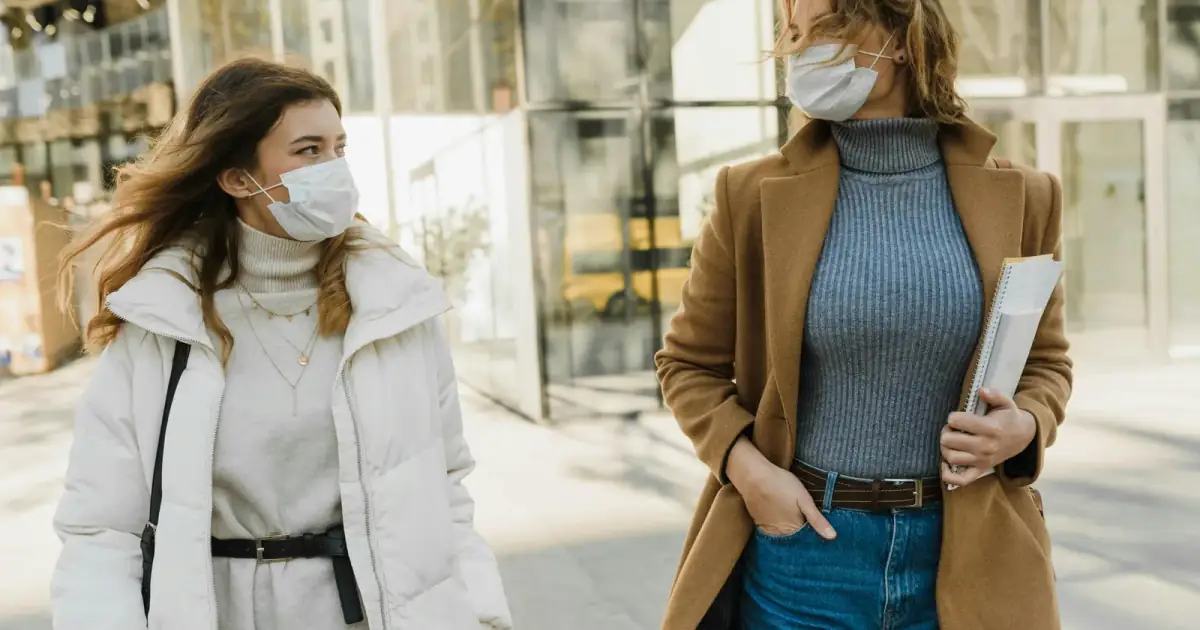 Two women wearing masks walking outdoors on a sunny day, embracing the new normal.