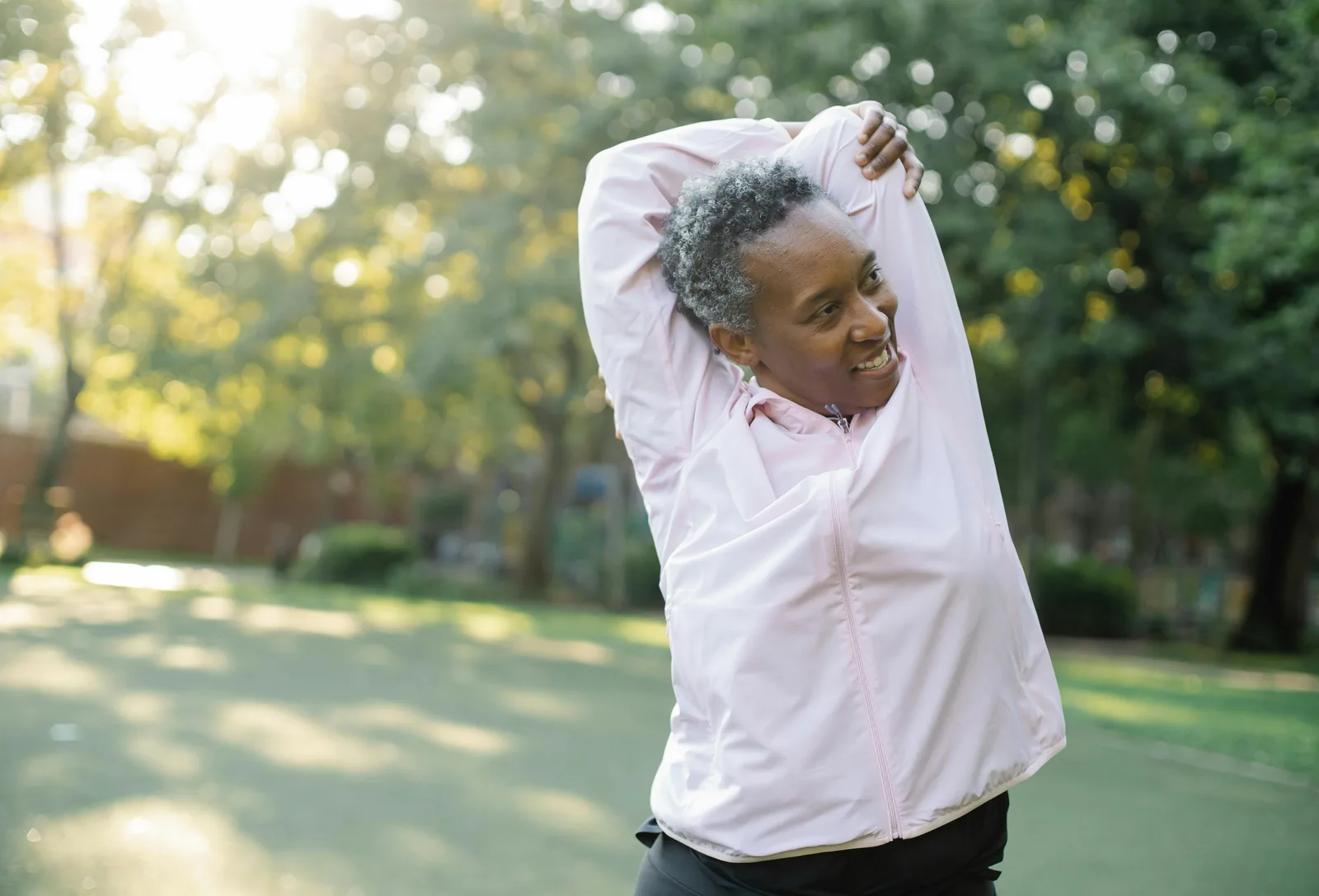 Specific lifestyle levers: Elderly African American woman doing stretching exercises outdoors in a park, embracing a healthy lifestyle.