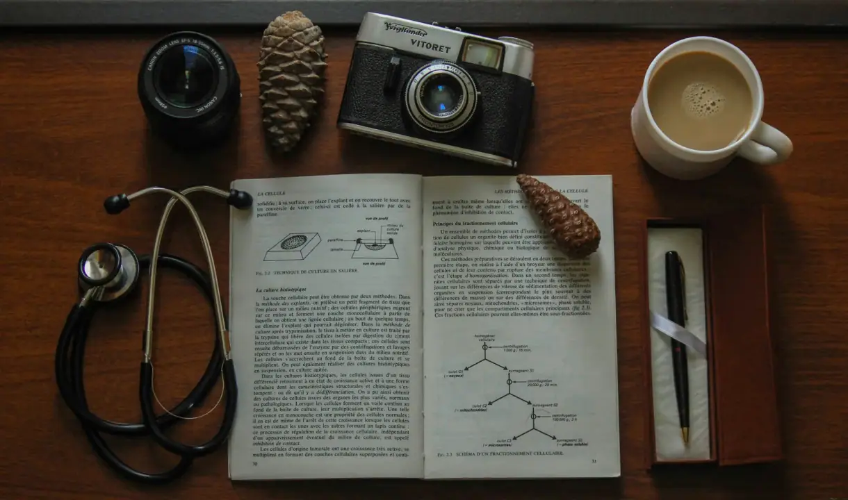 Counter-view: Top view of a vintage camera, open book, stethoscope, and coffee on a wooden table.