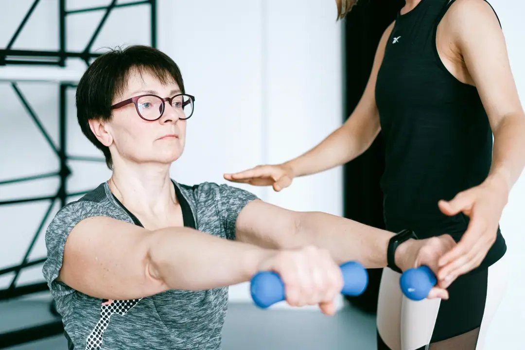 Evidence for HRV-guided training: A personal trainer guides a woman in exercising with dumbbells for fitness and strength training.