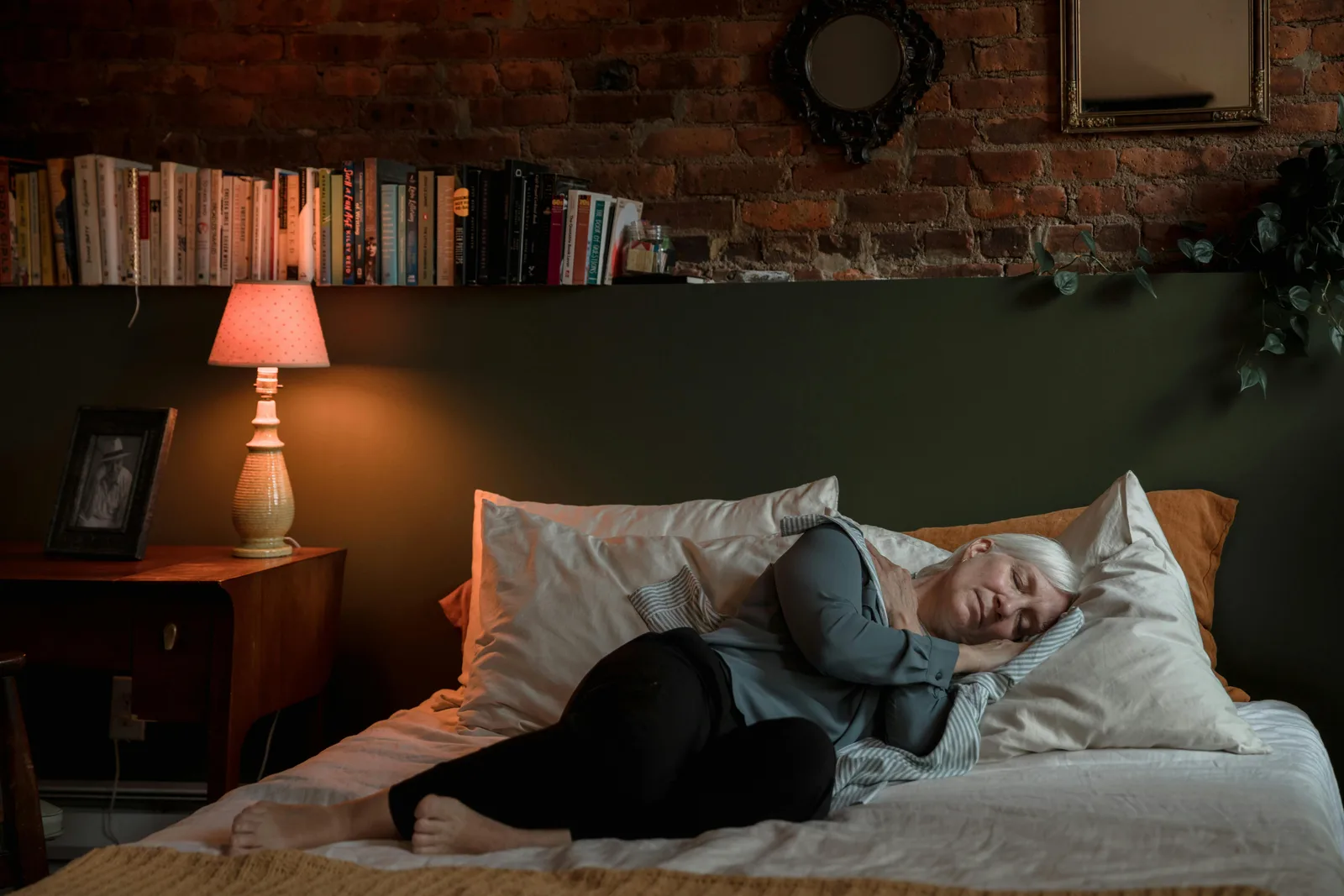 Stacking with other interventions: Elderly woman peacefully sleeping in a cozy bedroom with a lamp and books at night.