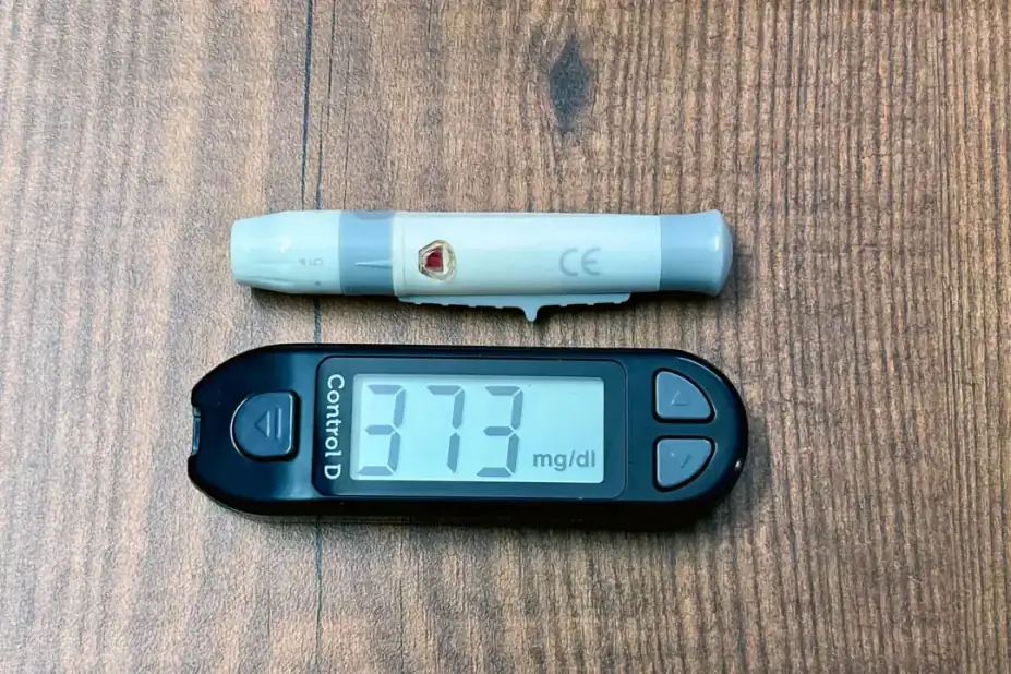 What does a high RDW mean?: A digital glucometer and lancing device on a wooden surface indicating high blood glucose level.
