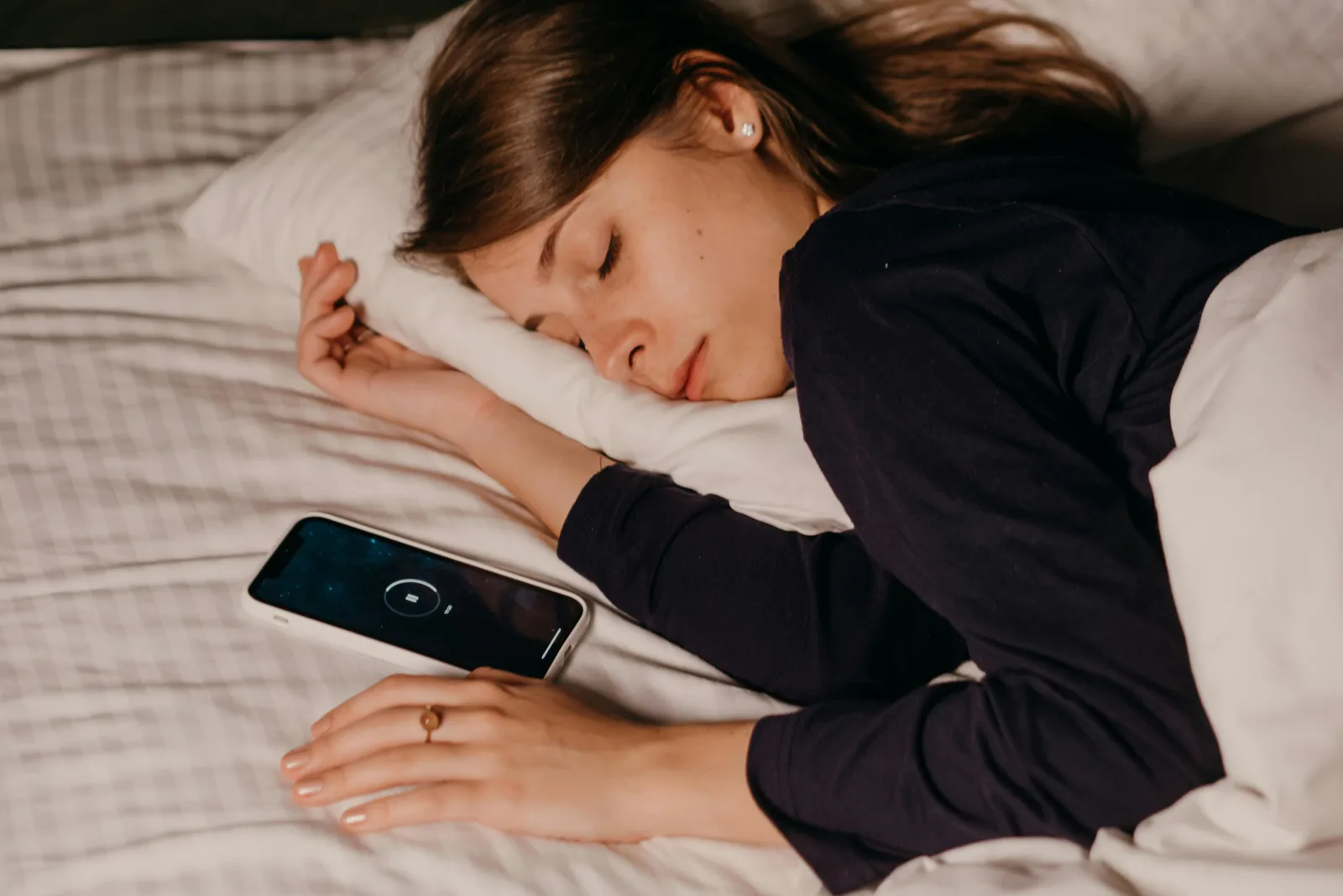 REM specifically and what wakes you up at 3 am: A woman peacefully sleeping in bed with a smartphone nearby, conveying rest and relaxation.