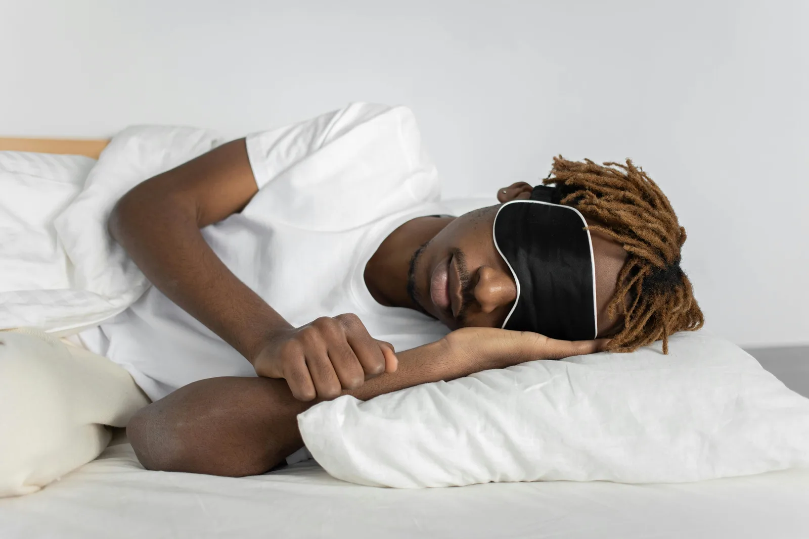 Which levers actually change sleep architecture?: A relaxed African American man sleeping in bed wearing a black sleep mask, promoting restful sleep.