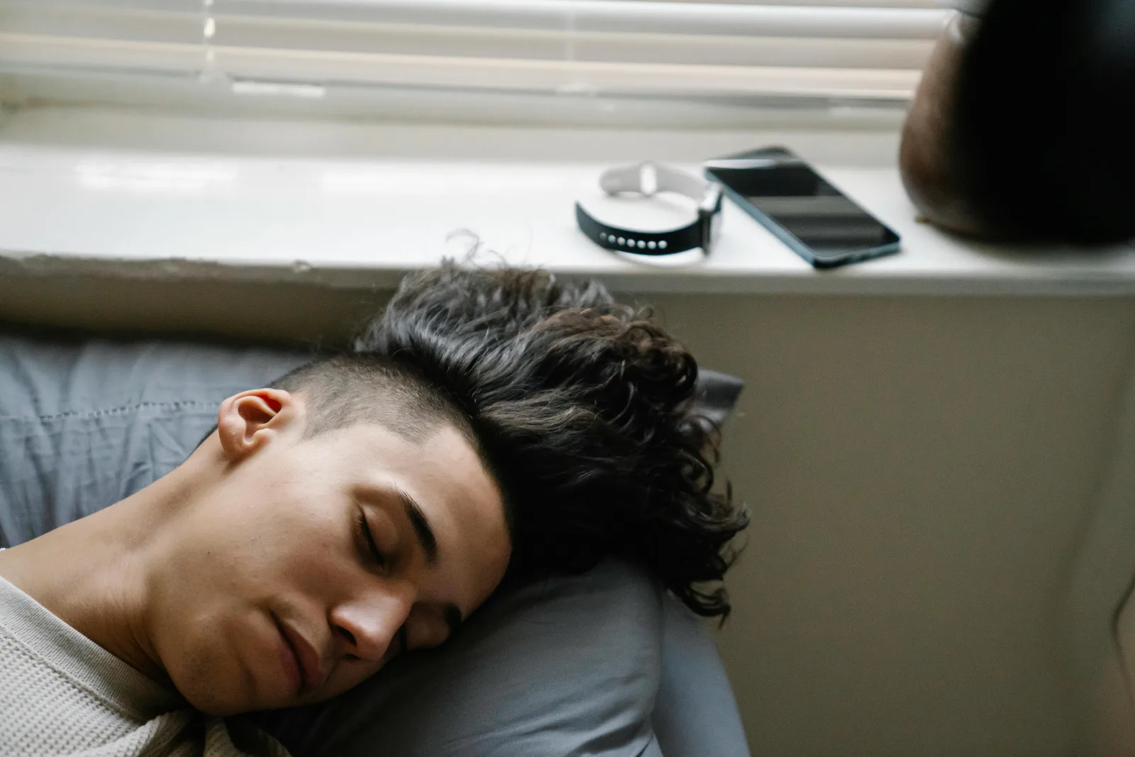 The four columns that matter: High angle of young Hispanic male with curly hair lying on bed near windowsill and sleeping in morning at home