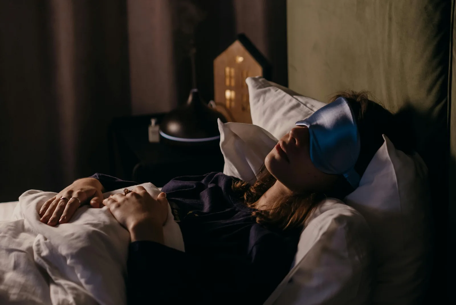 When should you cut caffeine and alcohol for better sleep?: A woman resting with a sleep mask in a calm bedroom setting, creating a serene and cozy atmosphere.