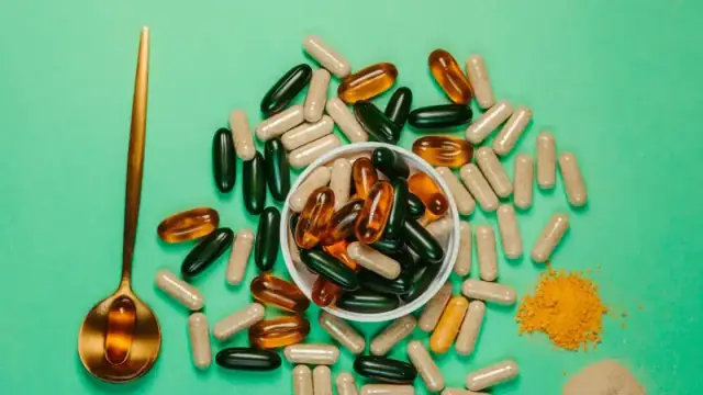 A vibrant assortment of capsules and powders on a green background with a golden spoon.