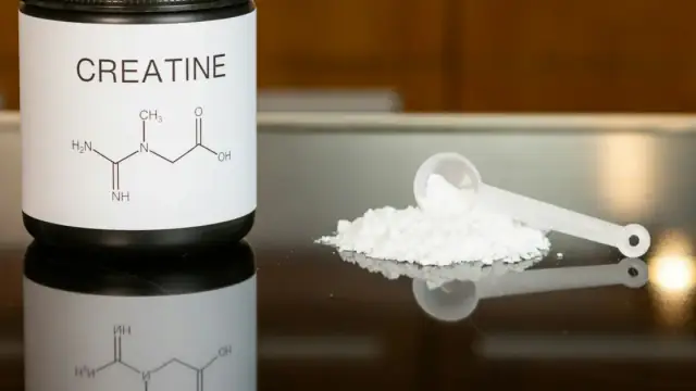 a bottle of creatine next to a spoon on a table
