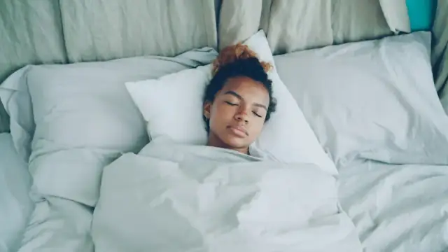 A young woman sleeping peacefully in a white bed.