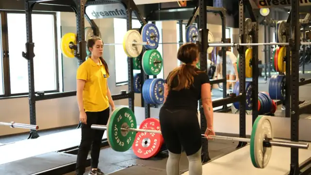 Two women weightlifting in a modern gym with colorful plates, showcasing fitness training.