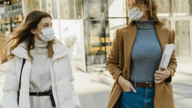 Two women wearing masks walking outdoors on a sunny day, embracing the new normal.