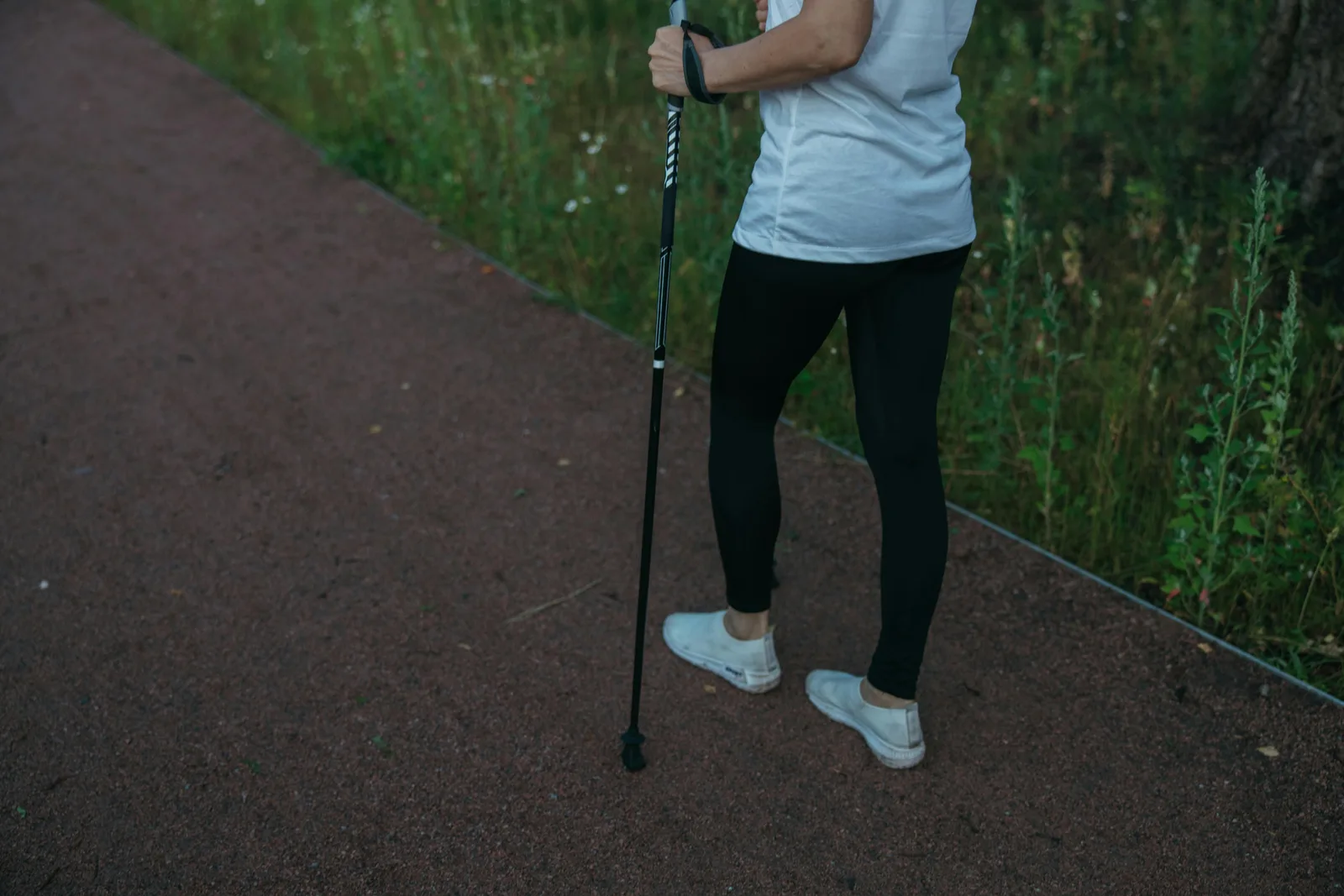 Why is walking better than other cardio for longevity?: A person in athletic wear uses a trekking pole while walking on a forest pathway.